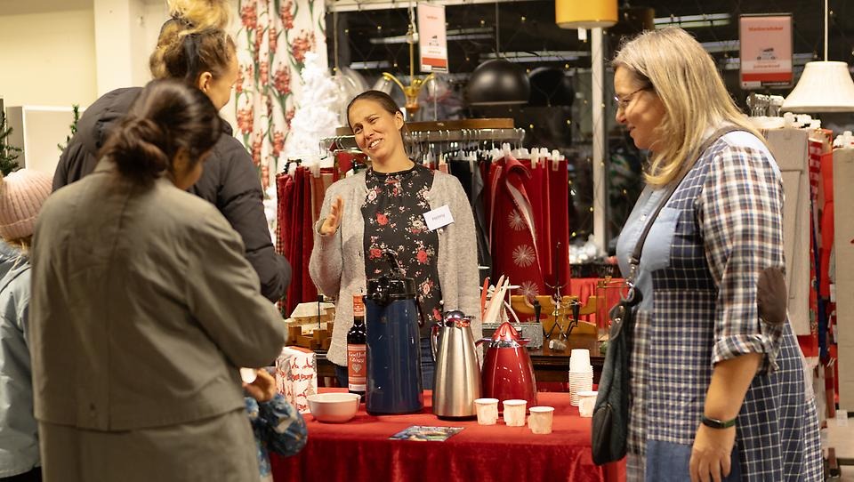 Kvinna skrattar och bjuder kunder på glögg och pepparkakor.