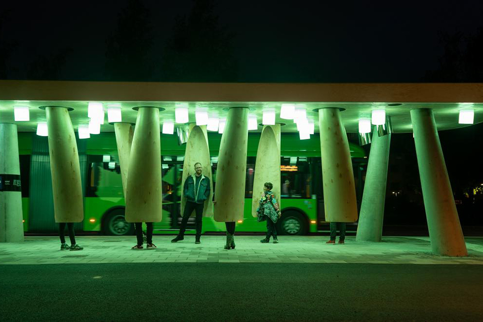 The image show a couple of people wainting for the bus at the bus stop a Station of Being