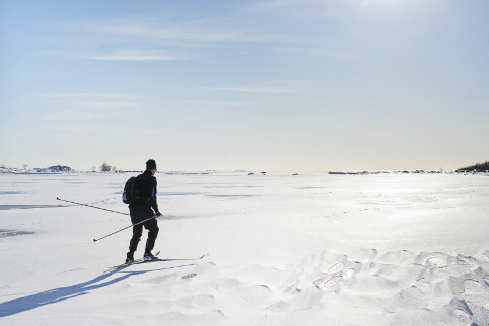 En skidåkare åker på snö över ett fruset hav. I bakgrunden syns lite träd från en strandkant i närheten.