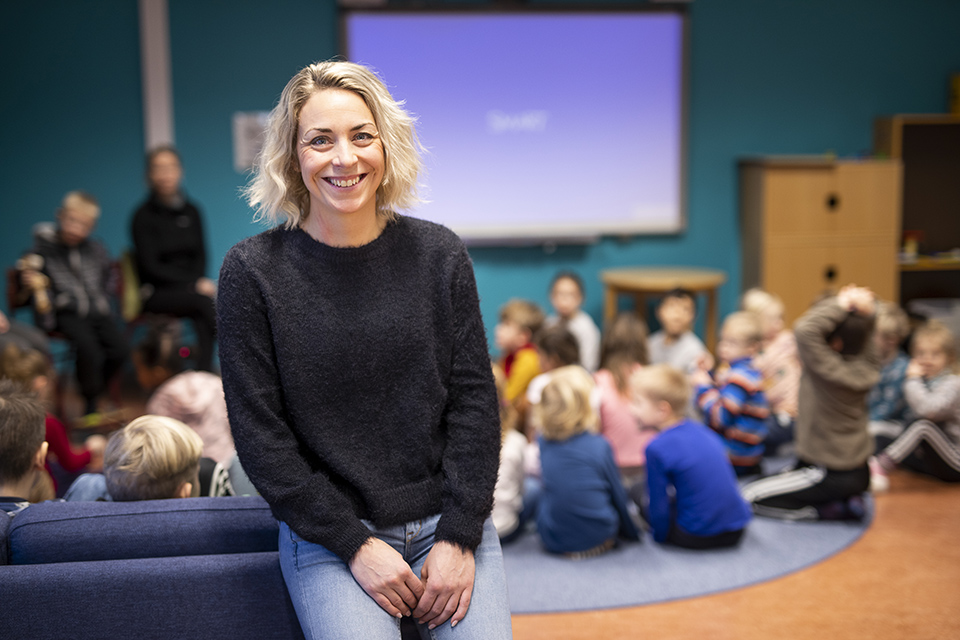 Kvinna som sitter på soffa med lågstadieelever i bakgrunden