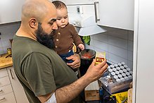Man med en liten pojke i famnen håller i tändsticksaskar i ett kök.