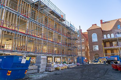 Byggarbetsplats med flervåningsflygel till vänster och Vasaskolan i rött tegel och med stora fönster till höger, omgivet av byggställningar och material.